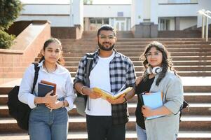 Portrait of three multi-ethnic university students embracing together standing in the campus photo