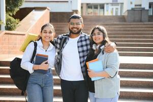 Portrait of three multi-ethnic university students embracing together standing in the campus photo
