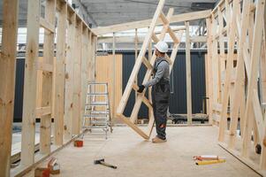 A worker or engineer in a uniform works on a construction site for the manufacture of wooden modular houses photo