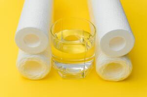 Water filters. Carbon cartridges and a glass on a yellow background. Household filtration system photo