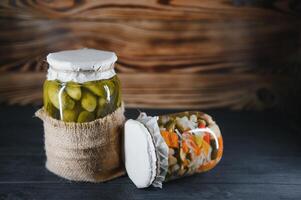 Glass jars with pickled cucumbers pickles, pickled tomatoes and cabbage. Jars of various pickled vegetables. Canned food in a rustic composition. photo