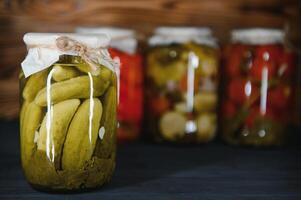 Glass jars with pickled cucumbers pickles, pickled tomatoes and cabbage. Jars of various pickled vegetables. Canned food in a rustic composition. photo