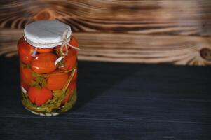 Homemade pickled tomatoes in glass jars on rustic wooden background. Fermented tomatoes in transparent glass. Homemade canned tomatoes. photo