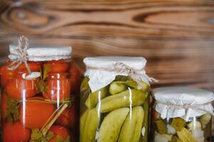 Canned cucumbers and tomatoes with craft lids on a wooden background. Cucumbers and tomatoes with place for text. Stocks of canned food. Harvest, stocks for the winter. photo