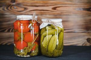Canned cucumbers and tomatoes with craft lids on a wooden background. Cucumbers and tomatoes with place for text. Stocks of canned food. Harvest, stocks for the winter. photo