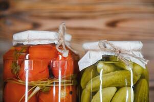 Canned cucumbers and tomatoes with craft lids on a wooden background. Cucumbers and tomatoes with place for text. Stocks of canned food. Harvest, stocks for the winter. photo