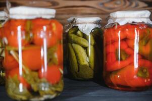 Glass jars with pickled cucumbers pickles, pickled tomatoes and cabbage. Jars of various pickled vegetables. Canned food in a rustic composition. photo