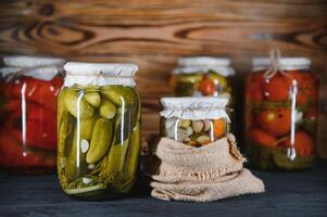 Canned cucumbers and tomatoes with craft lids on a wooden background. Cucumbers and tomatoes with place for text. Stocks of canned food. Harvest, stocks for the winter. photo