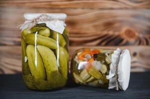 Glass jars with pickled cucumbers pickles, pickled tomatoes and cabbage. Jars of various pickled vegetables. Canned food in a rustic composition. photo