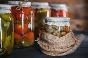 Glass jars with pickled cucumbers pickles, pickled tomatoes and cabbage. Jars of various pickled vegetables. Canned food in a rustic composition. photo