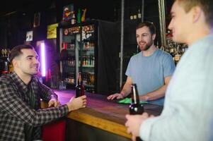 Two young men in casual clothes are smiling and talking while sitting at bar counter in pub photo