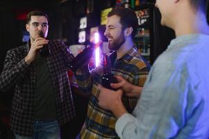 Young men in casual clothes are talking, laughing and drinking while sitting at bar counter in pub photo