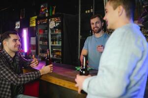 Two young men in casual clothes are smiling and talking while sitting at bar counter in pub photo
