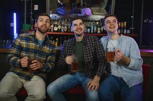 Young men in casual clothes are talking, laughing and drinking while sitting at bar counter in pub photo