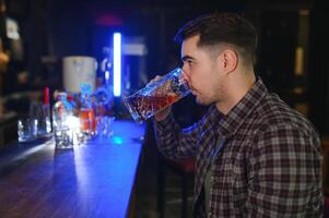 Handsome bearded man drinking beer at the bar counter in pub photo