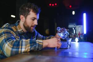 Sad young man sitting at bar counter in pub. Upset man drinks alcohol because of problems at work. photo