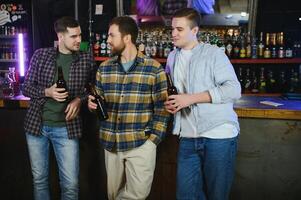 Young men in casual clothes are talking, laughing and drinking while sitting at bar counter in pub photo