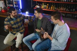 Old friends meeting. Happy young men in casual wear toasting with beer while sitting in beer pub together photo