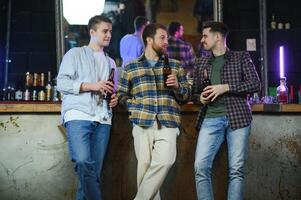Young men in casual clothes are talking, laughing and drinking while sitting at bar counter in pub photo