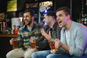 Soccer fans cheering for favourite team while enjoying drinks. Group of supporters celebrating victory while watching football match on tv in a club. Happy friends shouting while cheering for a goal. photo