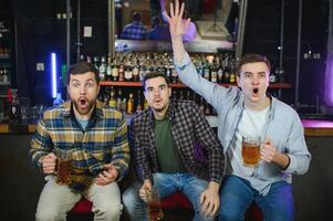 Soccer fans cheering for favourite team while enjoying drinks. Group of supporters celebrating victory while watching football match on tv in a club. Happy friends shouting while cheering for a goal. photo