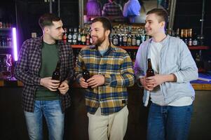 Young men in casual clothes are talking, laughing and drinking while sitting at bar counter in pub photo