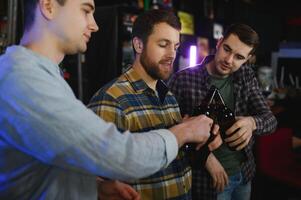 Young men in casual clothes are talking, laughing and drinking while sitting at bar counter in pub photo