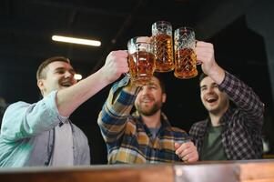 Soccer fans cheering for favourite team while enjoying drinks. Group of supporters celebrating victory while watching football match on tv in a club. Happy friends shouting while cheering for a goal. photo