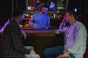 Two young men in casual clothes are smiling and talking while sitting at bar counter in pub photo