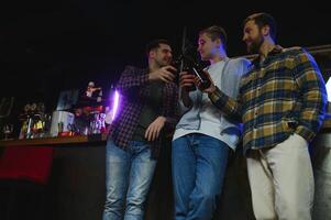 Young men in casual clothes are talking, laughing and drinking while sitting at bar counter in pub photo