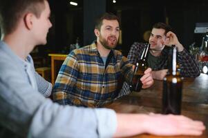 Young men in casual clothes are talking, laughing and drinking while sitting at bar counter in pub photo