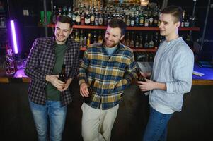 Young men in casual clothes are talking, laughing and drinking while sitting at bar counter in pub photo