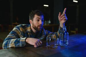 Sad young man sitting at bar counter in pub. Upset man drinks alcohol because of problems at work. photo