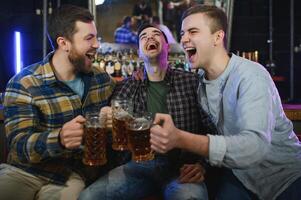 Young men in casual clothes are talking, laughing and drinking while sitting at bar counter in pub photo