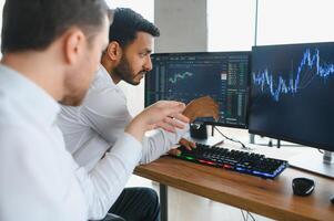 Two successful trader sitting in office and looking at screen, checking cryptocurrency information data on finance market graph, pointing on monitor photo