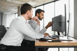 Two successful trader sitting in office and looking at screen, checking cryptocurrency information data on finance market graph, pointing on monitor photo