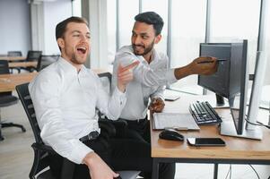 Two men traders sitting at desk at office together monitoring stocks data candle charts on screen analyzing price flow smiling cheerful having profit teamwork concept photo