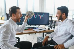 Two successful trader sitting in office and looking at screen, checking cryptocurrency information data on finance market graph, pointing on monitor photo