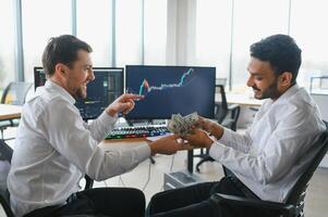 Two successful trader sitting in office and looking at screen, checking cryptocurrency information data on finance market graph, pointing on monitor photo