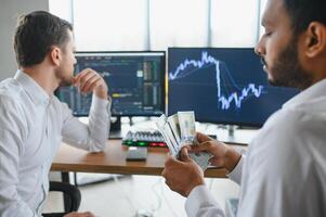 Two successful trader sitting in office and looking at screen, checking cryptocurrency information data on finance market graph, pointing on monitor photo