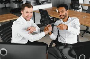 Two men traders sitting at desk at office together monitoring stocks data candle charts on screen analyzing price flow smiling cheerful having profit teamwork concept photo