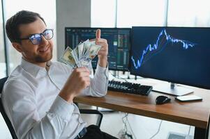 Man trader in formalwear sitting at desk in frot of monitors with charts and data at office browsing laptop checking documents analyzing stocks price changes concentrated. photo
