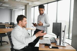 Two successful trader sitting in office and looking at screen, checking cryptocurrency information data on finance market graph, pointing on monitor photo