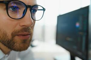 Young business man trader wearing glasses looking at computer screen with trading charts reflecting in eyeglasses watching stock trading market financial data growth concept, close up. photo