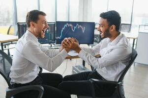 Two successful trader sitting in office and looking at screen, checking cryptocurrency information data on finance market graph, pointing on monitor photo
