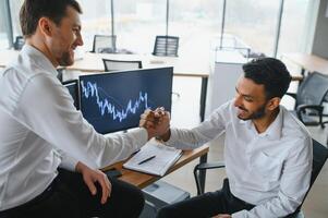 Two successful trader sitting in office and looking at screen, checking cryptocurrency information data on finance market graph, pointing on monitor photo