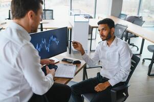 Two successful trader sitting in office and looking at screen, checking cryptocurrency information data on finance market graph, pointing on monitor photo