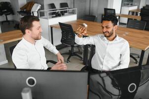 Two men traders sitting at desk at office together monitoring stocks data candle charts on screen analyzing price flow smiling cheerful having profit teamwork concept photo