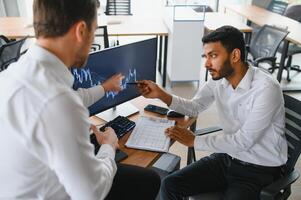 Two men traders sitting at desk at office together monitoring stocks data candle charts on screen analyzing price flow smiling cheerful having profit teamwork concept photo