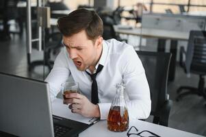 Alcoholism at work. Tired employee drinking alcohol at workplace, can not handle stress. photo